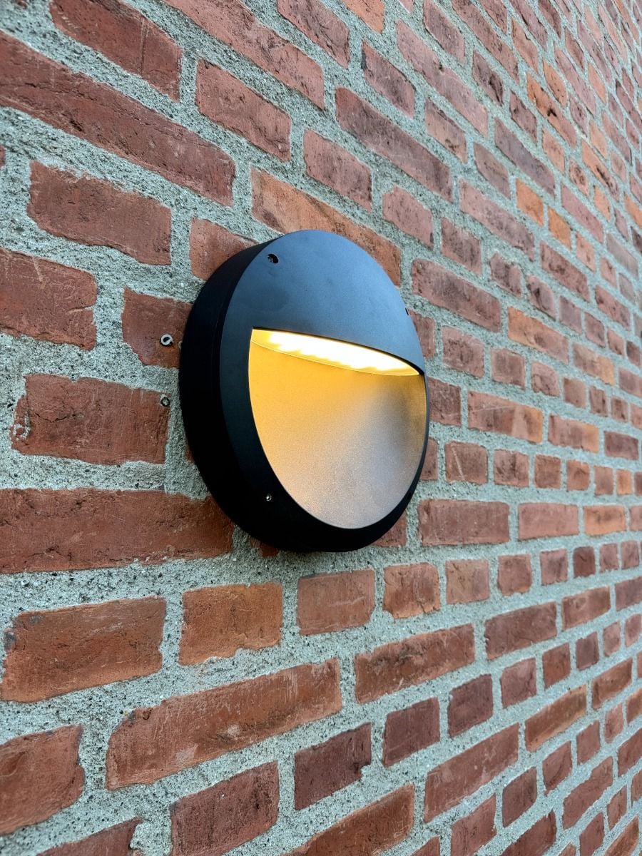 Sort ALED Luna CCT LED-væglampe tændt på murstensfacade